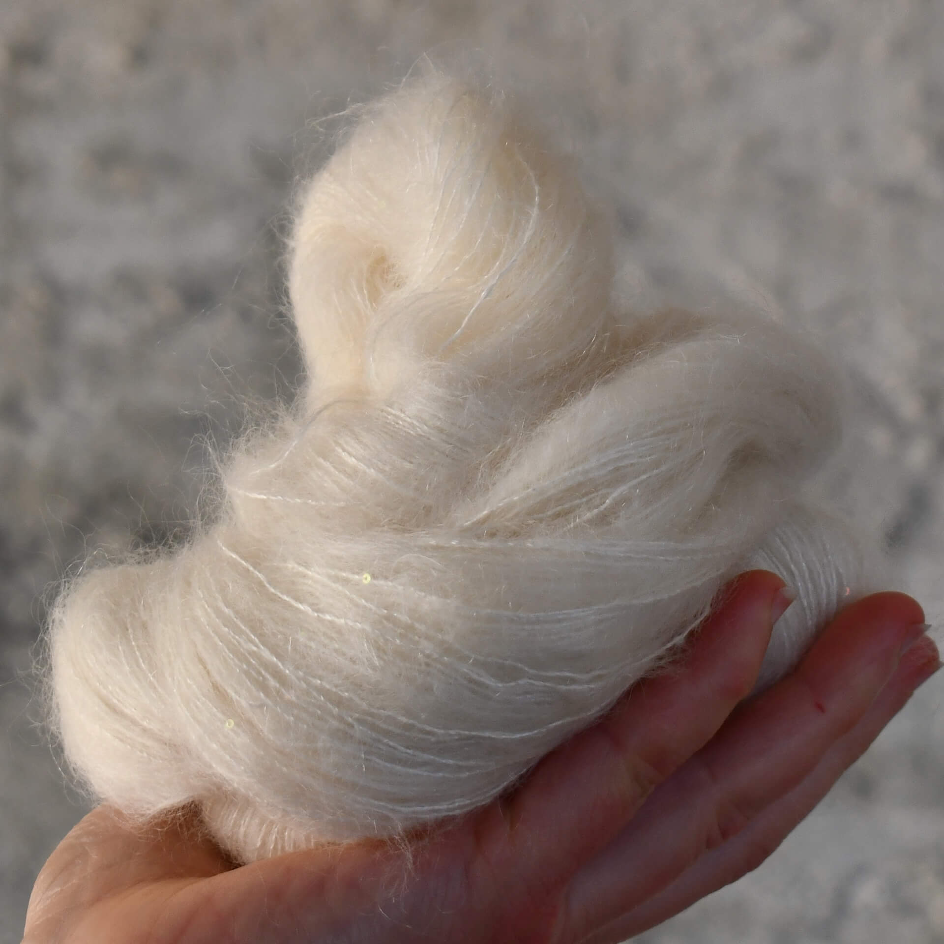 A skein of kid silk sequin undyed yarn. It is fluffy and has tiny shiny sequins in it